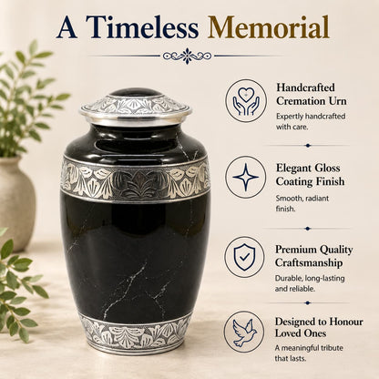Black cremation urn with silver detailing on a light wooden surface, surrounded by greenery.