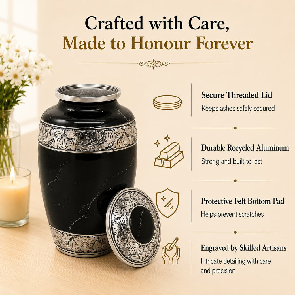 Black urn with silver detailing on a wooden surface, surrounded by flowers and a candle.