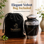 Black marble urn with silver detailing and a black velvet bag on a wooden surface, featuring TrueHaven Memorials branding.