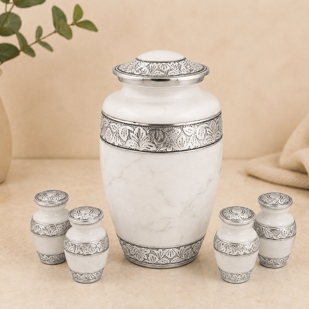 A white marble-style cremation urn with ornate silver-toned metal bands and a matching lid, shown with four smaller matching urns arranged around it on a beige surface.